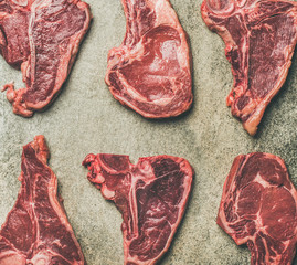 Flat-lay of fresh raw uncooked beef meat steak cuts over grey concrete background, top view....