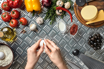 Set of ingredients for pizza and baker's hand smash eggs on metal table