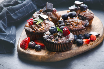 Fresh, blueberry muffins with strawberry, chocolate on a wooden board and stone background with sugar and fruits. Food background. Concept of pastry. 