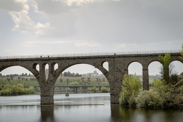Fototapeta na wymiar Old stone bridge for railroad crossing a dam next to a highway 