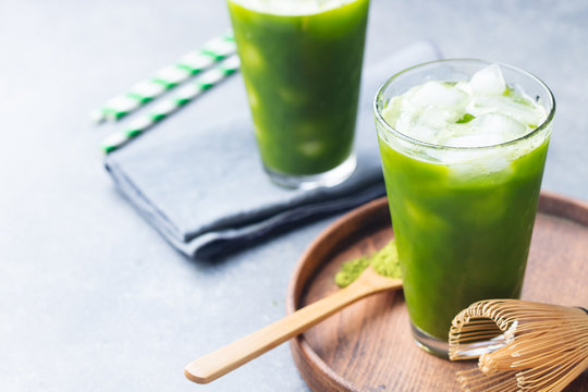 Matcha, green tea ice tea in tall glass on wooden plate. Grey stone background.