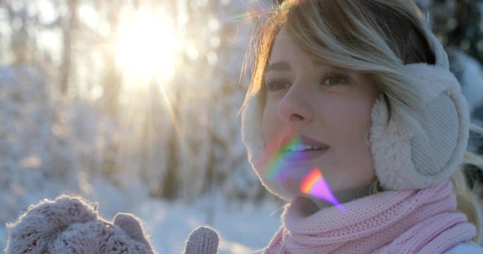 Portrait of young girl wearing a winter white pullover and pink scarf trying to warm herself in winter park. Nice weather, sun is shining.