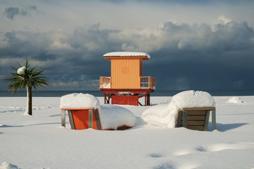Snow covered lifeguard tower, branches and a palm tree on a beach