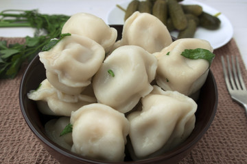 Appetizing dumplings with meat close-up, greens of parsley and pickled cucumbers in the background.