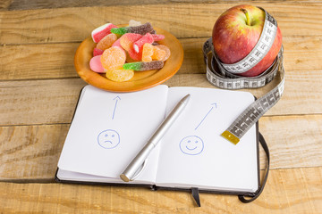 Apple with measuring tape, jelly beans and notebook on wooden table