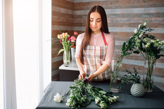 Fototapeta Female florist at work: pretty young dark-haired woman making fashion modern bouquet of different flowers. Women working with flowers in workshop