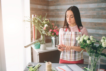 Female florist at work: pretty young dark-haired woman making fashion modern bouquet of different flowers. Women working with flowers in workshop