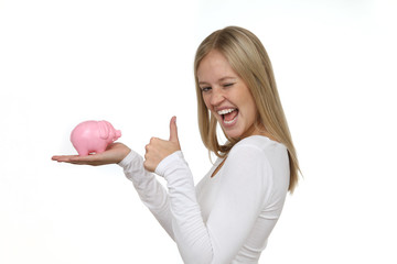 Hübsche blonde Frau begeistert hält ein Sparschwein in ihrer Hand und Daumen hoch 