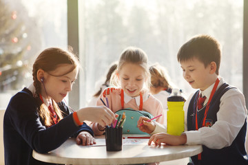Schoolchildren draw with colored pencils sitting at the table
