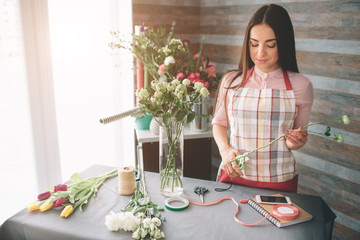 Female florist at work: pretty young dark-haired woman making fashion modern bouquet of different flowers. Women working with flowers in workshop