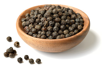 dried black peppercorns in the wooden plate, isolated on white