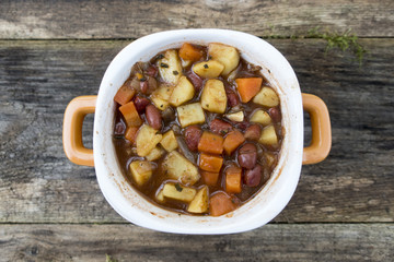 Appetizing beautiful soup with potatoes, onions, carrots and beans. On an old wooden background and close-up. View from above.