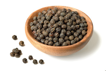 dried black peppercorns in the wooden plate, isolated on white