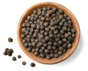 dried black peppercorns in the wooden plate, isolated on white, top view.