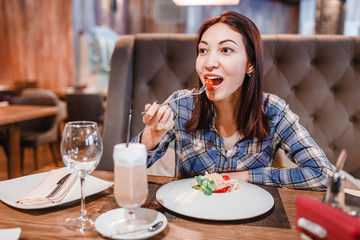Eastern woman eating spaghetti pasta with fork in luxury restaurant