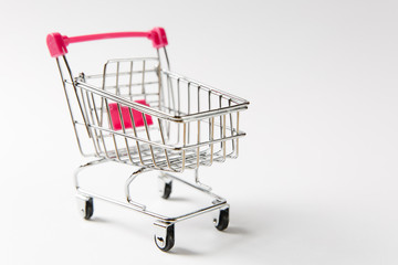 Close up of supermarket grocery push cart for shopping with black wheels and pink plastic elements on handle isolated on white background. Concept of shopping. Copy space for advertisement