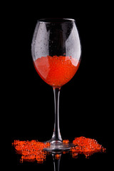Red caviar in a glass scattered on a black background