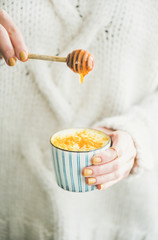 Healthy vegan turmeric latte or golden milk with honey in hands of woman wearing white sweater