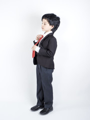 Shot of a cute little boy in a business suit holding a red tie, on a gray background