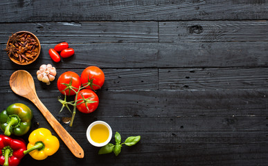 Top view of a wooden table full of italian pasta ingradients like peppers, tomatoes, olive oil, basi