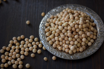 Soybeans in metal plate over black wooden background.