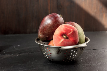 Mango and peach fruits in metal colander