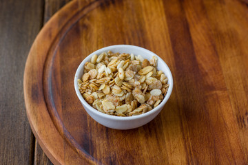 Granola or muesli in white ceramic bowl over wooden table.