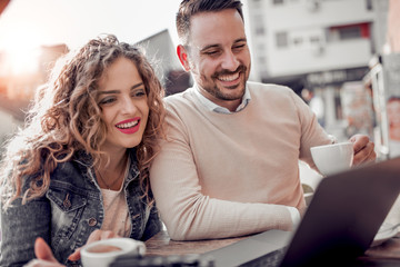 Happy couple at coffee shop looking at laptop.