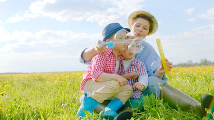 Little boys and their mother are blowing bubbles at flowering field on summertime
