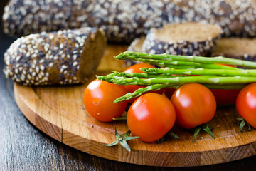 Fresh and ripe asparagus and cherry tomatoes with bread on wooden board.