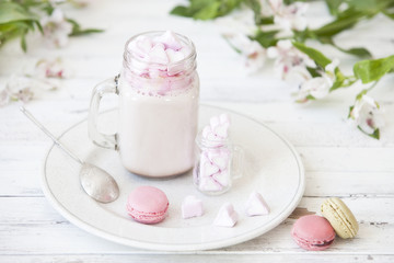 Close-up of tasty milkshake in glass cup with sweet pink macarons on plate near white flowers. Close-up of tasty milkshake in glass cup with sweet pink macarons on plate near white flowers. Close-up, 