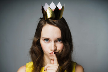 lovely beautiful blue-eyed girl in a yellow dress put a finger to her lips, a crown on her head