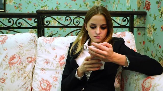 Young business woman in suit uses smartphone on the sofa