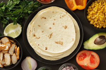 Tacos ingredients background with flatbread, fresh vegetables and roasted chicken meat on the table.