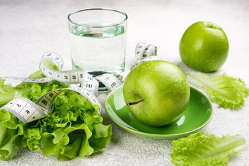 Healthy food. Green apple, lettuce salad, glass of water, measuring tape on white background. Dieting, slimming, healthy eating concept