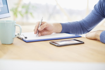 Businessman doing some paperwork. Close-up of businessman's hand writing somesthing on the paper. Casual professional man sitting at desk and fill the form.