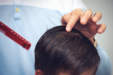 Fototapeta premium Hairdresser's hands making hairstyle to child. Close view.