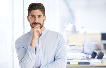 Naklejka premium Confident young businessman portrait. Portrait of a casual young man standing at office, looking at camera and smiling. 