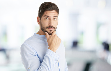 Obraz premium Young man thinking. Portrait shot of a handsome businessman with hand on chin standing at the office and thinking about his business idea.