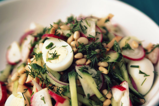 Quail eggs salad in the white bowl. Healthy lunch. European cuisine. Close up. Radish, cucumber, quail eggs and pine nuts. Ovo vegetarian dish.