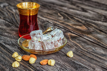 Turkish joys with different nuts is a glass of tea and a spoon. Eastern sweets. Traditional Turkish delight (Rahat lokum) on a wooden background. View from above .