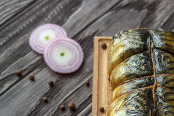 Mackerel smoked fish on a wooden background, close-up, next lemon onion pea pepper, top view.
