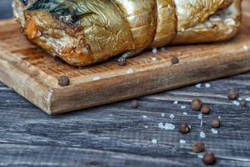 Mackerel smoked fish on a wooden background, close-up, next lemon onion pea pepper, top view.