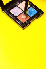 Brush for make-up over a set of eye shadow on yellow background. Copy space