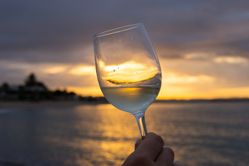 Female hand with a glass of white wine on the background of a beautiful sunset.  Travel vacations concept.
