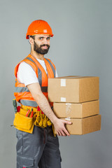 A man-builder in an orange helmet with a cardboard box in his hands. On a gray background