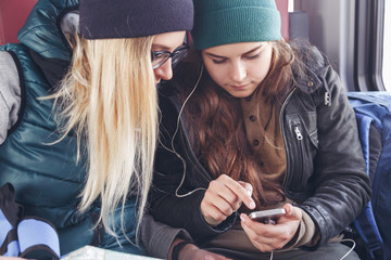 Couple of female friends looking at the smartphone while on the train