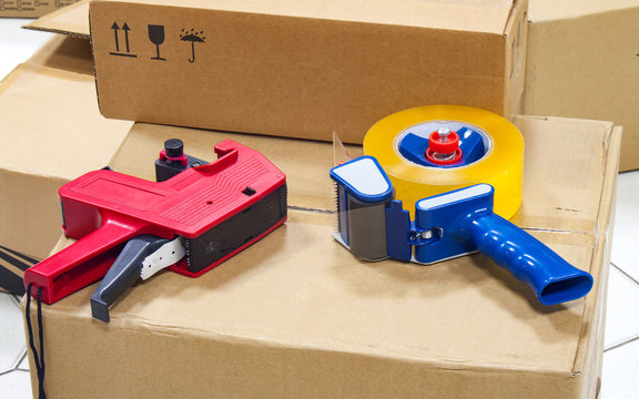 Packing tape dispenser and label gun on the cardboard box.