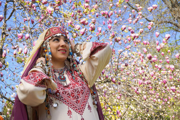 Girl against of magnolia flowers in national Palestinian costume, with head covered. 