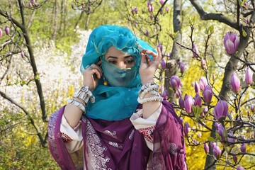 Obraz premium Girl against of magnolia flowers in national Palestinian costume, with head covered. 